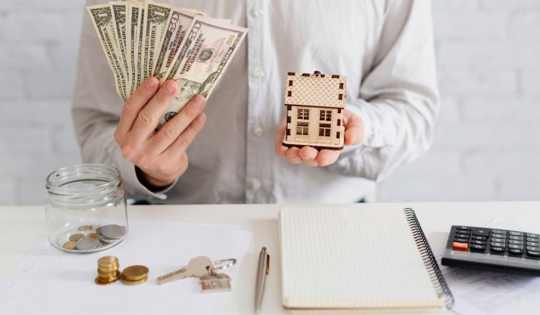 A homeowner holding cash and a miniature house while planning for an FHA mortgage application.