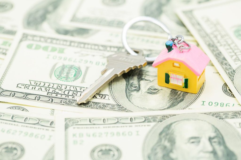 House keys and a model home on a bed of dollar bills representing FHA mortgage loan requirements.