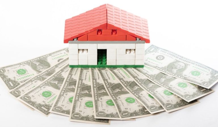 A LEGO house sits on a fan of one-dollar bills, symbolizing home equity used for a cash-out refinance.