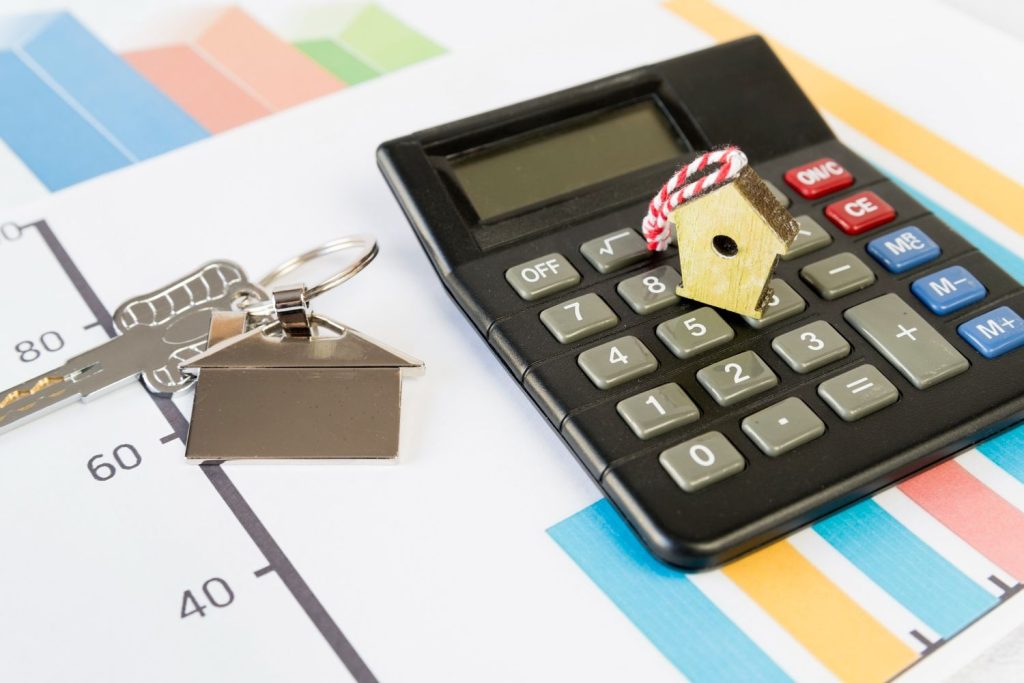 Calculator with a small birdhouse and house keys on a financial graph representing mortgage interest costs.