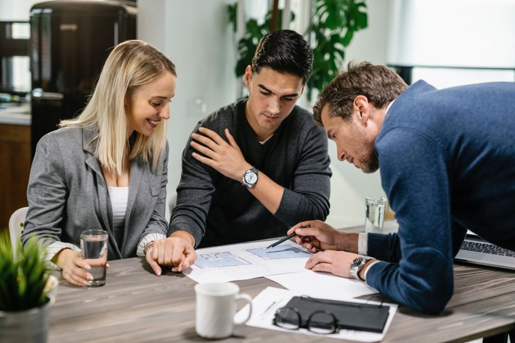 A mortgagor couple reviews house plans with a mortgagee representative to discuss loan terms and property details.