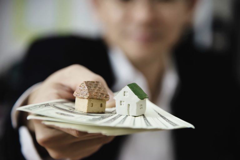 A person holding cash and small houses, symbolizing the payout benefits of a reverse mortgage for seniors.