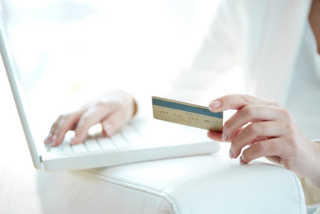 Person holding a credit card at a laptop, reviewing statement balance vs current balance online.