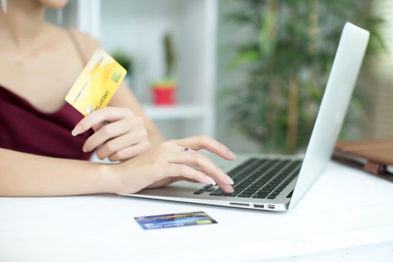 Woman holding a credit card while checking statement balance vs current balance on a laptop.