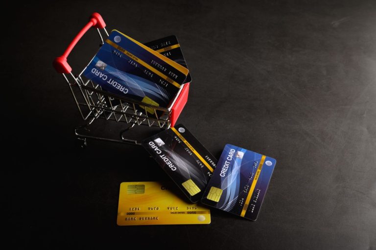 Multiple credit cards inside and around a miniature shopping cart, illustrating how to choose the best credit cards for groceries to maximize cash back and rewards.