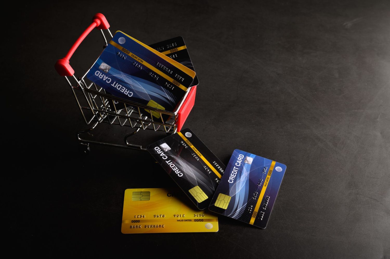 Multiple credit cards inside and around a miniature shopping cart, illustrating how to choose the best credit cards for groceries to maximize cash back and rewards.