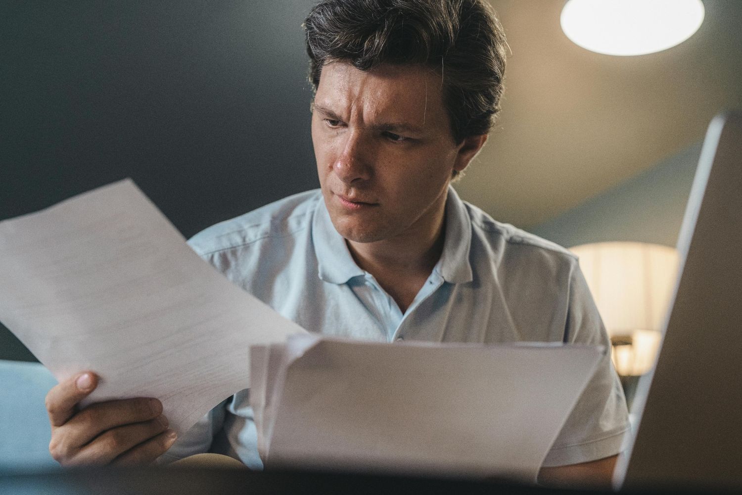 Man reviewing a debt validation letter with a worried expression near a laptop.
