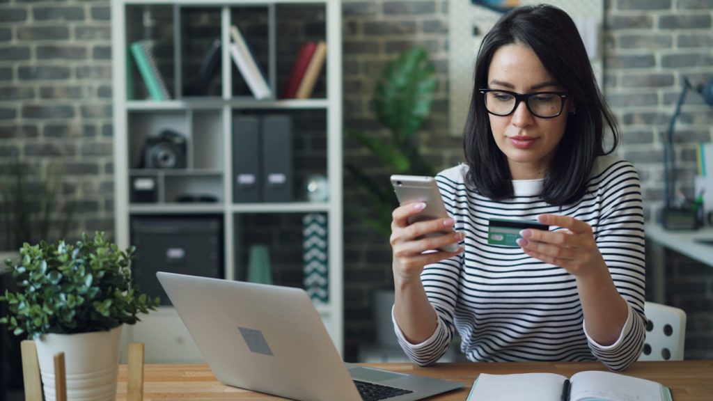 Woman reviewing her credit card and phone to check for charges before filing a chargeback.