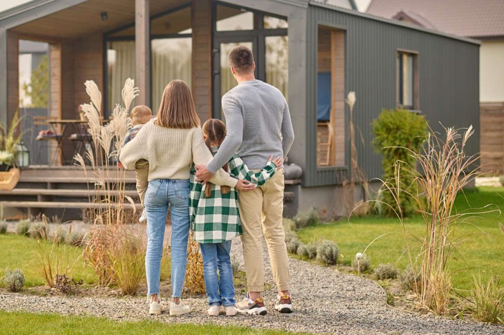 Family standing outside a modern timeshare home, viewing the property from a landscaped front yard.