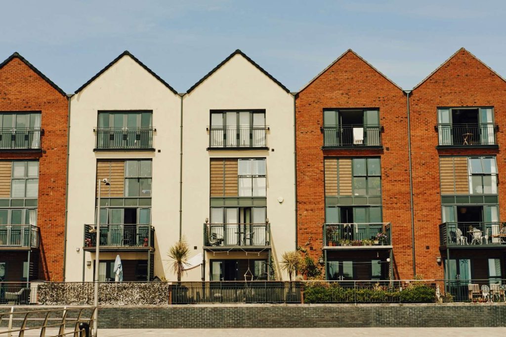 Row of brick and cream townhouse with balconies under blue sky.