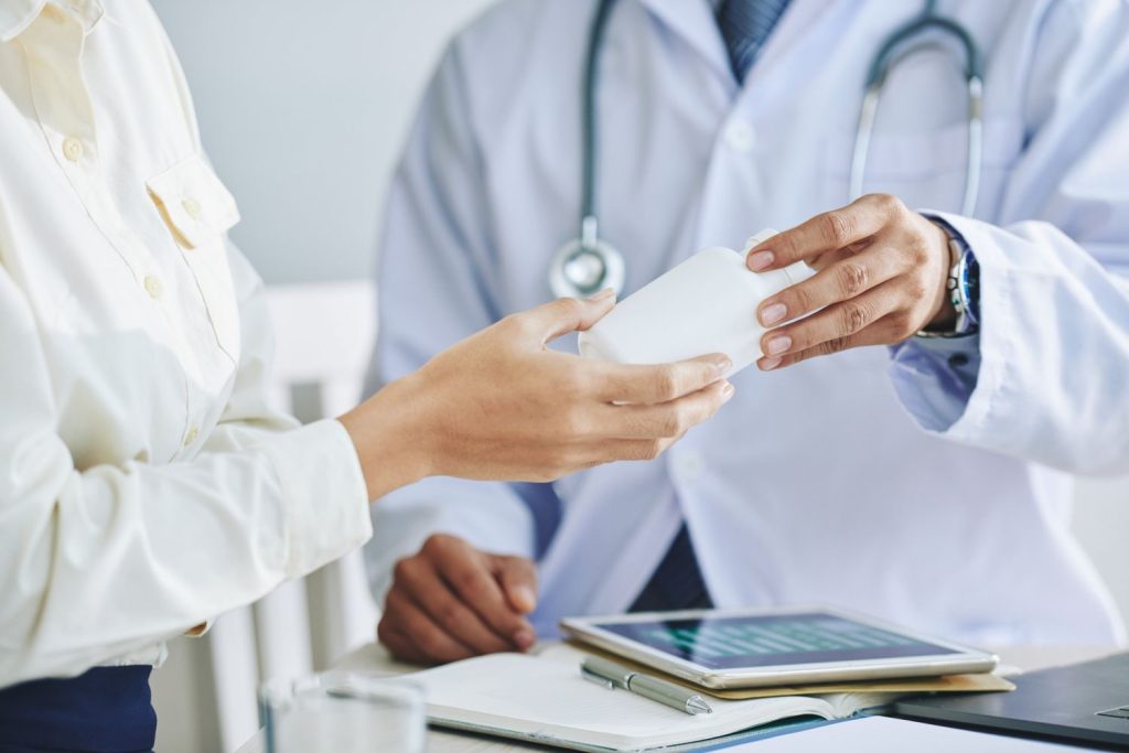 Doctor handing medication to a patient during a consultation about HDHP and PPO health insurance coverage.