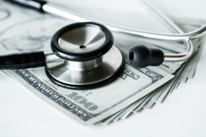 Stethoscope on cash illustrating healthcare costs and expenses related to Medicaid and Medicare coverage.