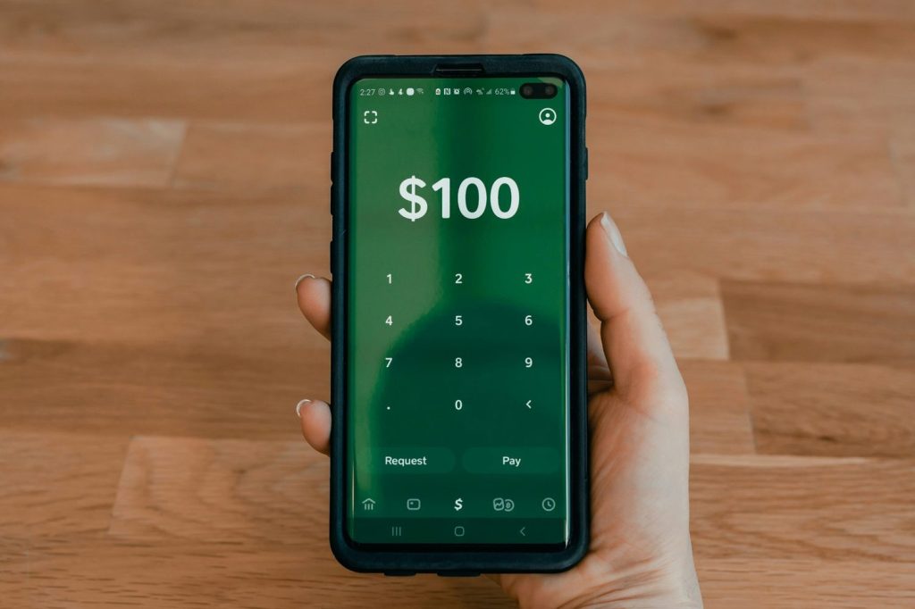 Hand holding a phone showing a $100 screen in an online savings account.