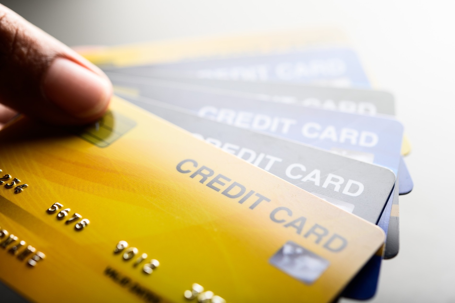 Hand holding several credit cards fanned out against a light background.