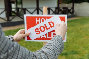 Person placing a sold sticker on a house listing sign, illustrating new home sales activity in the housing market.