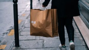 Person carrying a shopping bag on a city sidewalk, illustrating consumer spending and retail sales trends.