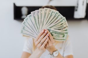 Rich person hiding face behind fanned US dollar bills of mixed denominations