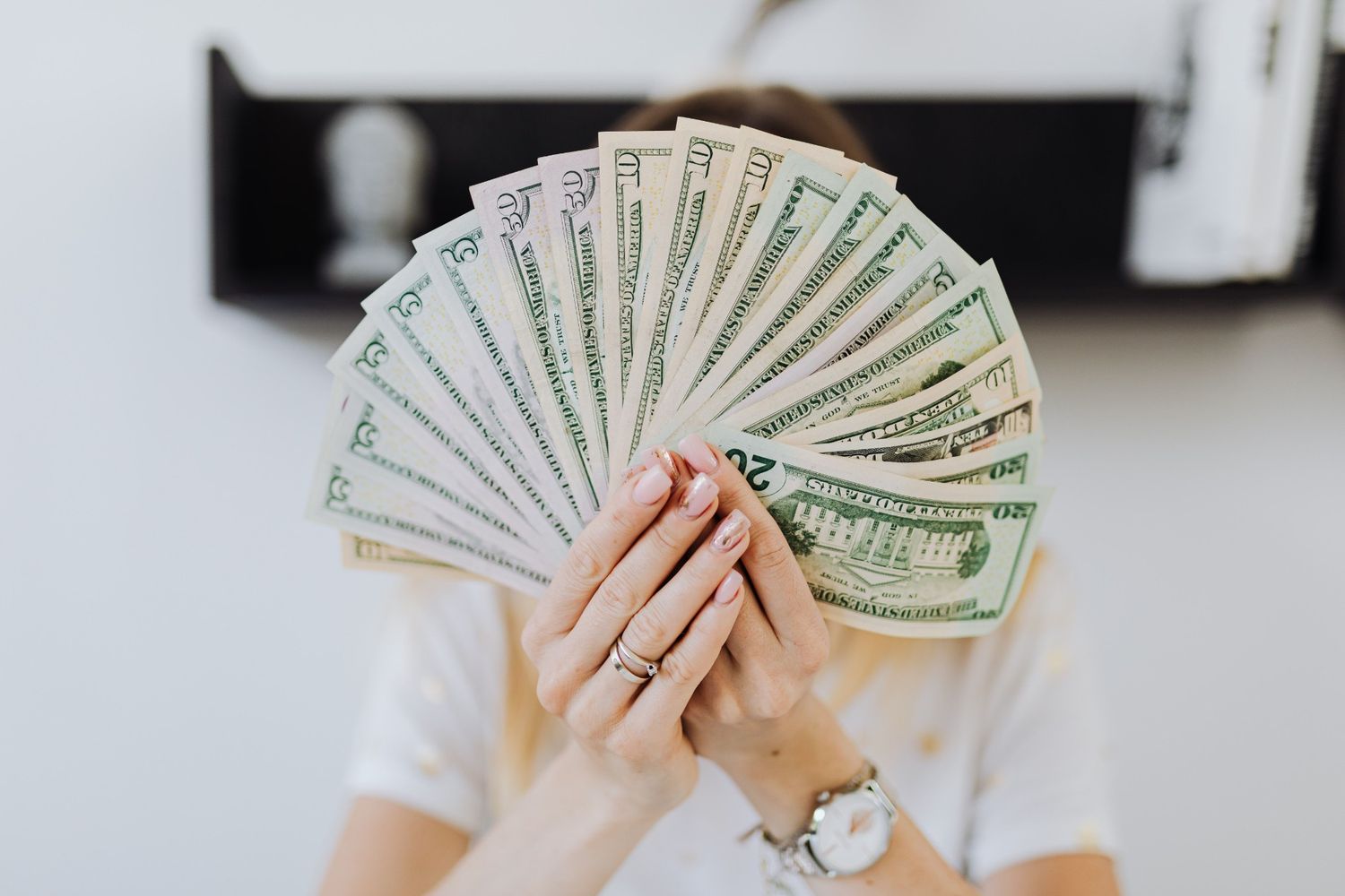 Rich person hiding face behind fanned US dollar bills of mixed denominations