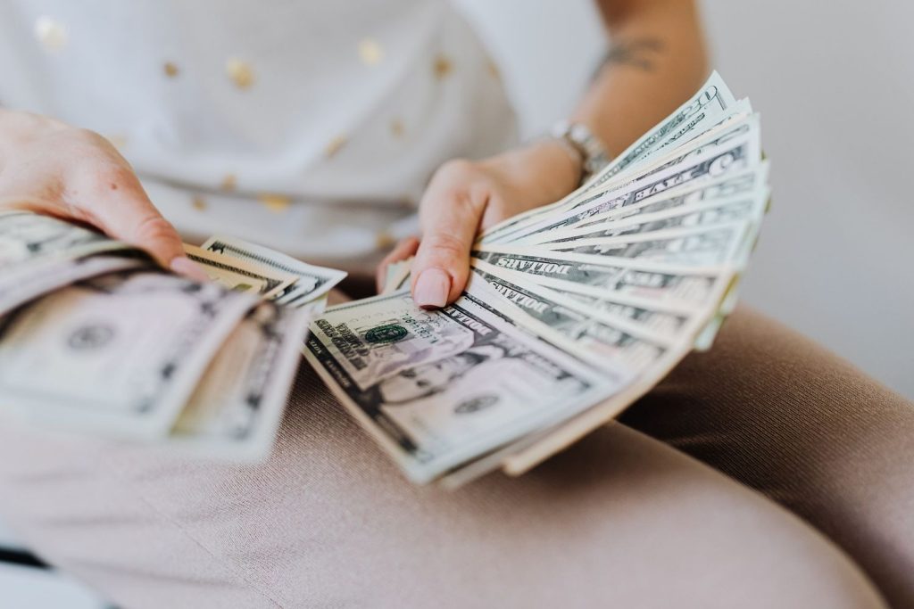 Woman counting rich stack of US dollar bills fanned out in hands.