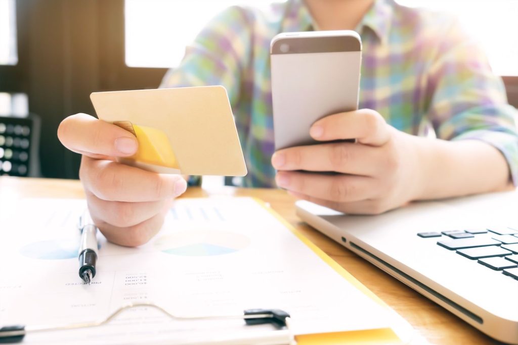 Person using a phone and credit card for payments while explaining what is a charge-off on a credit account.