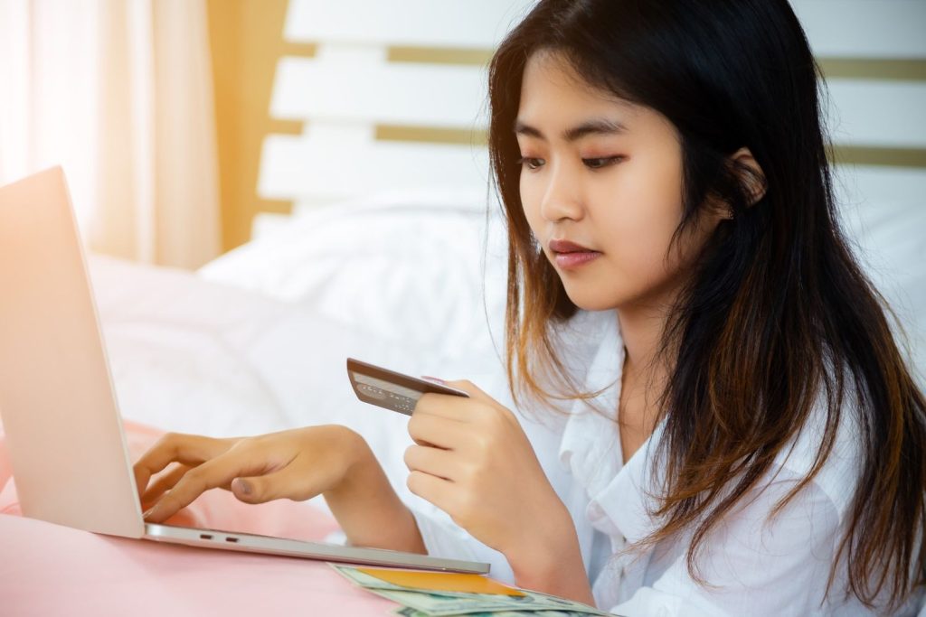 Person shopping online with a credit card and laptop, illustrating what is a charge-off after missed payments.