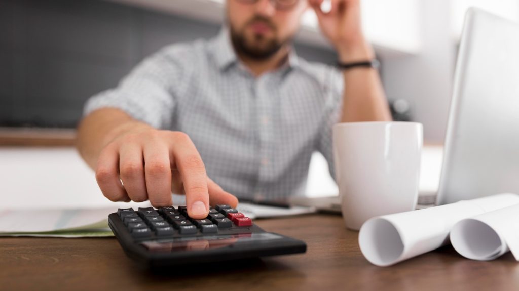 A man uses a calculator while reviewing finances and exploring debt consolidation to manage monthly payments.