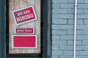 Storefront hiring sign illustrates rising jobless claims and changing employment opportunities in the local job market.