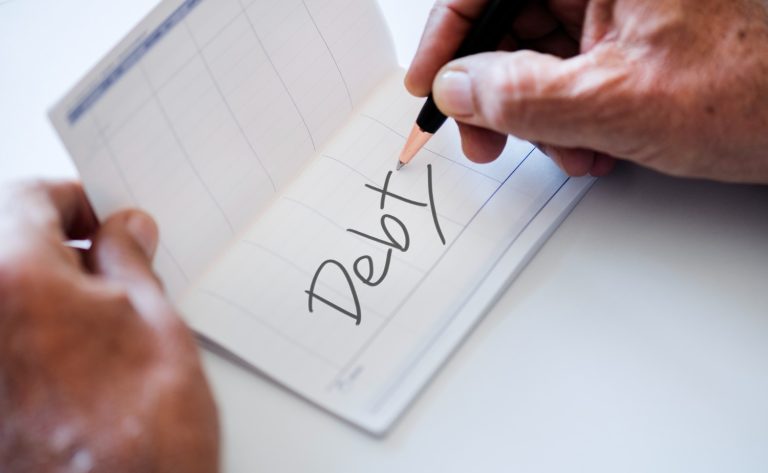 A person writes "Debt" in a checkbook while planning debt consolidation to organize outstanding balances.
